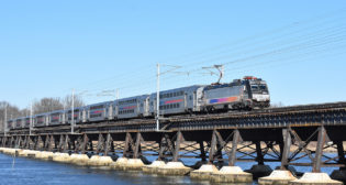 Westbound NJT North Jersey Coast Line train 3231—nine MultiLevels hauled by an ALP46 electric—crosses the Navesink River Bridge. Along the line is the Long Branch Station, where a USDOT Reconnecting Communities Pilot Program award will help remove an at-grade rail crossing and construct a pedestrian tunnel. (William C. Vantuono Photograph)
