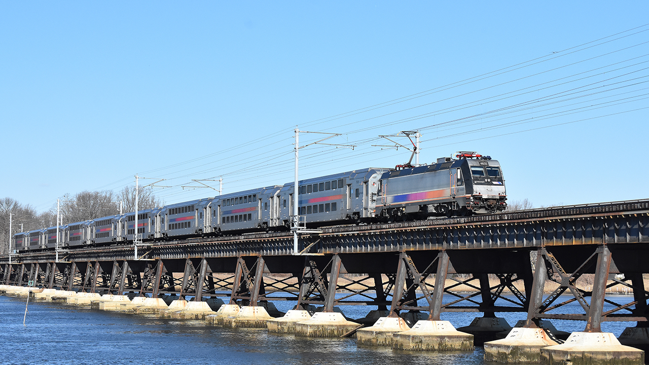 Westbound NJT North Jersey Coast Line train 3231—nine MultiLevels hauled by an ALP46 electric—crosses the Navesink River Bridge. Along the line is the Long Branch Station, where a USDOT Reconnecting Communities Pilot Program award will help remove an at-grade rail crossing and construct a pedestrian tunnel. (William C. Vantuono Photograph)